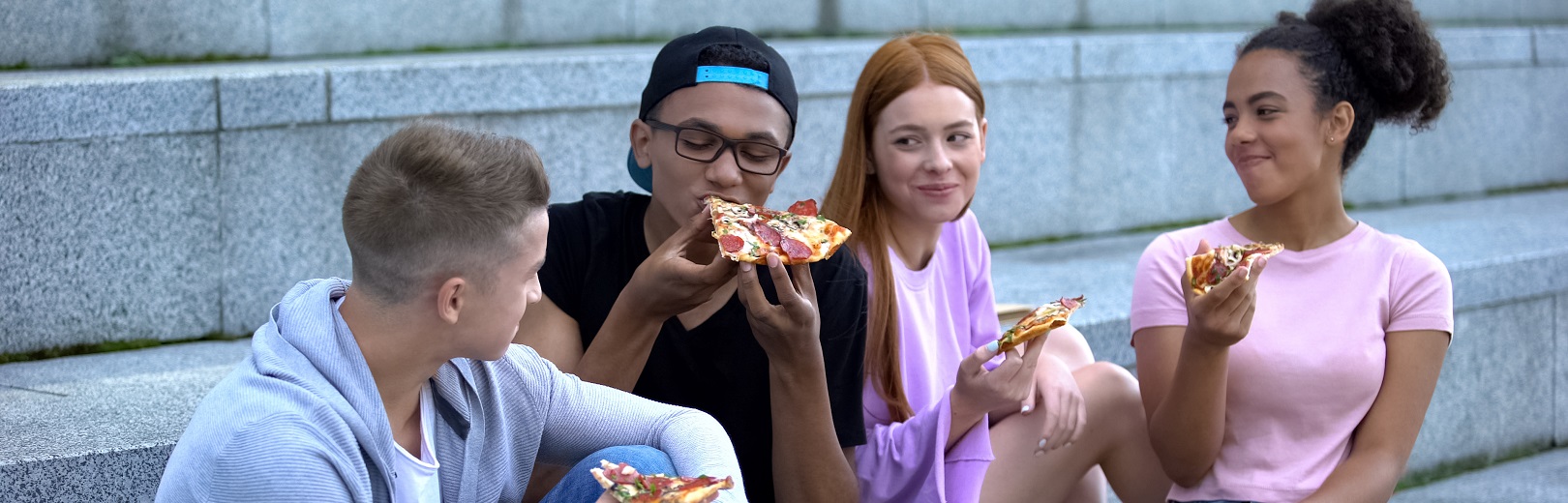 Four teenagers eating pizza on some outdoor stairs